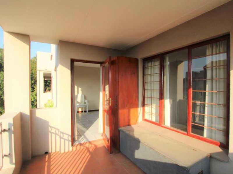 A covered balcony featuring tiled flooring, metal security bars on windows, and a built-in bench, providing a functional outdoor space.