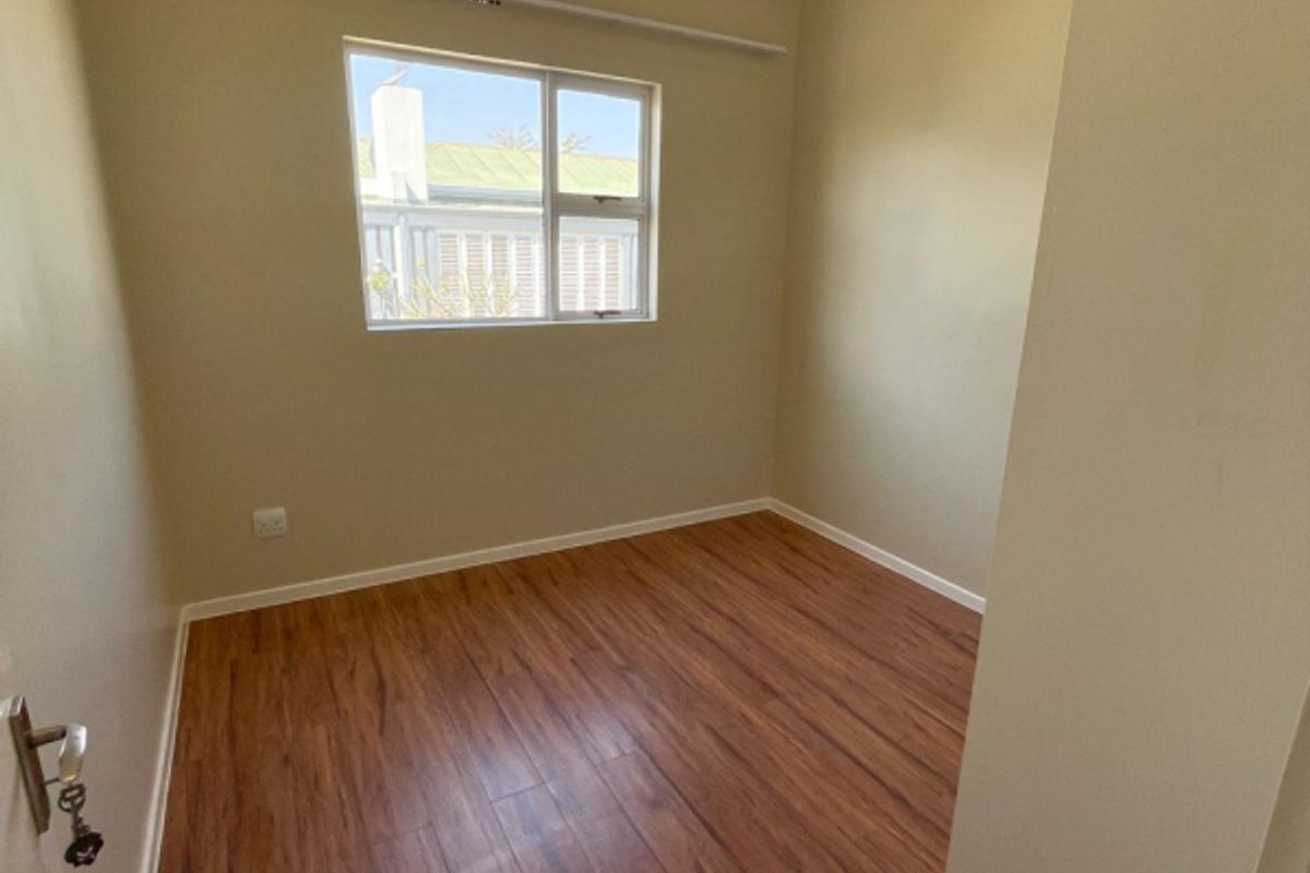 A clean, empty bedroom featuring warm-toned laminate flooring, recessed downlighting, and a neutral wall finish, ready for personalization.