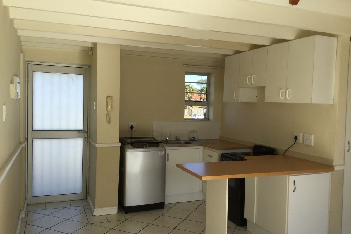 A functional kitchen featuring white cabinetry, laminate countertops, tiled flooring, and exposed ceiling beams, with direct access to an exterior door.