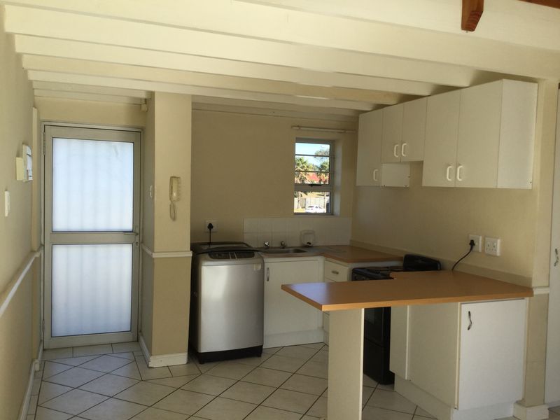 A functional kitchen featuring white cabinetry, laminate countertops, tiled flooring, and exposed ceiling beams, with direct access to an exterior door.