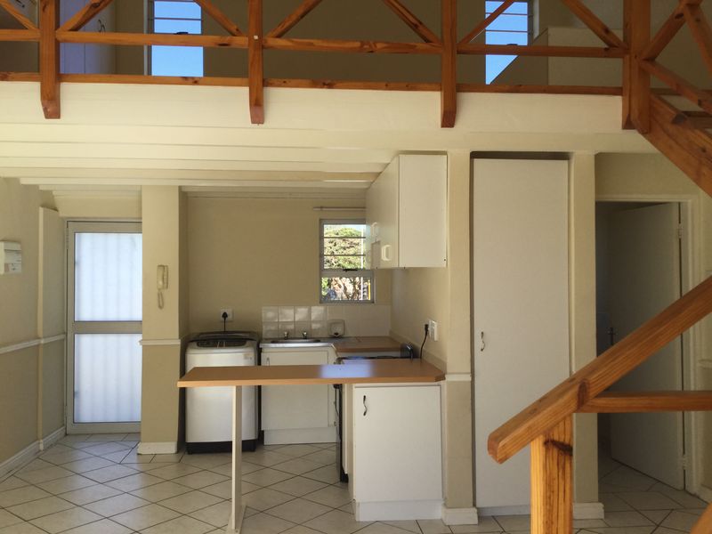 Open-plan kitchen and living area featuring a mezzanine level, wooden staircase, tiled flooring, and functional built-in cabinetry.