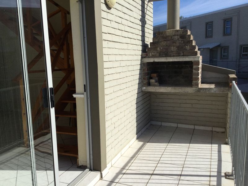 A private balcony featuring a built-in brick braai, tiled flooring, and a sliding glass door providing access to the interior.