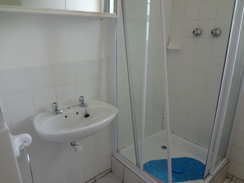 A compact bathroom featuring a wall-mounted basin and a glass-enclosed shower stall with white tiled finishes.
