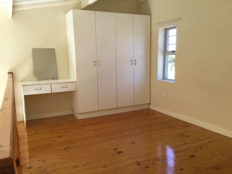 A bright bedroom featuring polished timber flooring, a built-in wardrobe, and an integrated vanity unit with a window providing natural light.