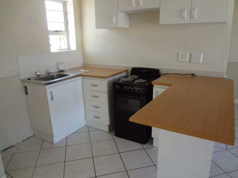 A compact, functional kitchen featuring white cabinetry, laminate countertops, a stainless steel sink, and a freestanding stove with tiled flooring.