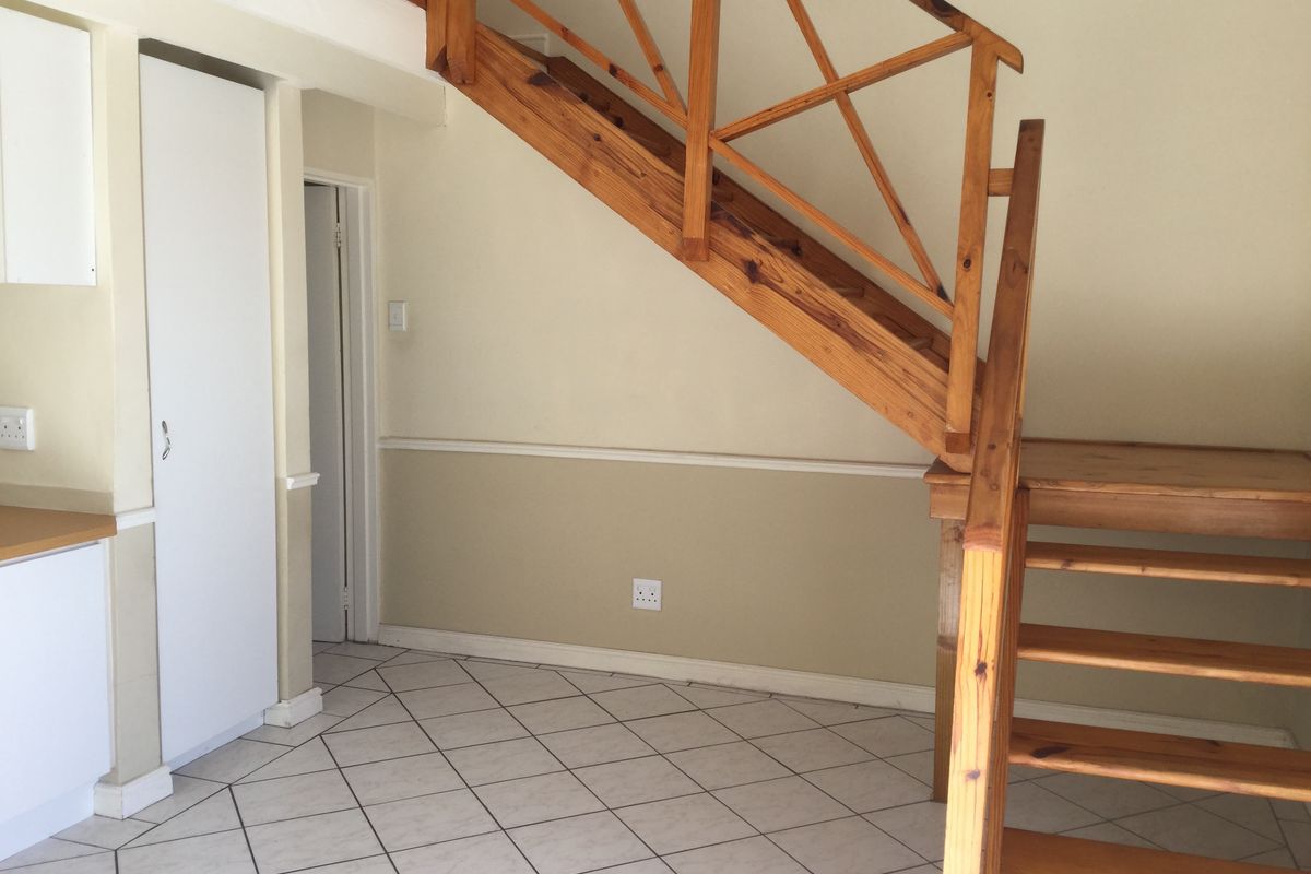 An open-plan living area featuring a wooden staircase, tiled flooring, and built-in cabinetry, presenting a functional space ready for modernization.