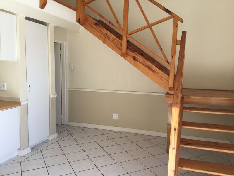 An open-plan living area featuring a wooden staircase, tiled flooring, and built-in cabinetry, presenting a functional space ready for modernization.