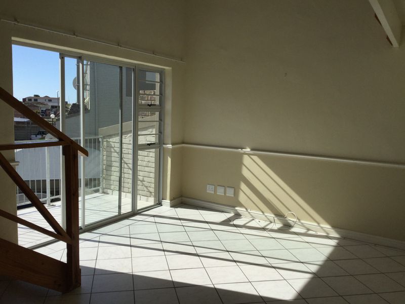 Bright and spacious living area featuring tiled flooring, a wooden staircase, and direct access to a private balcony through sliding glass doors.
