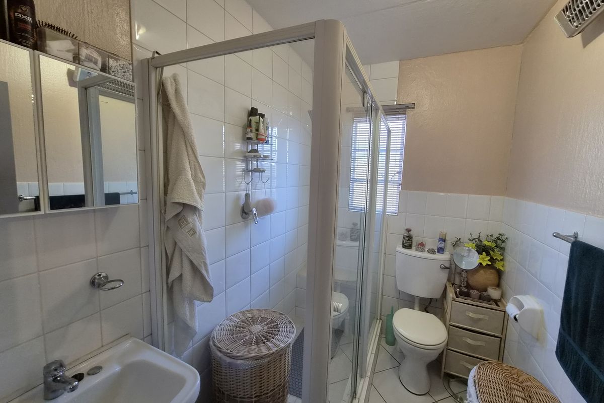 A functional bathroom featuring a shower enclosure, pedestal basin, and toilet with white wall tiling and tiled flooring.