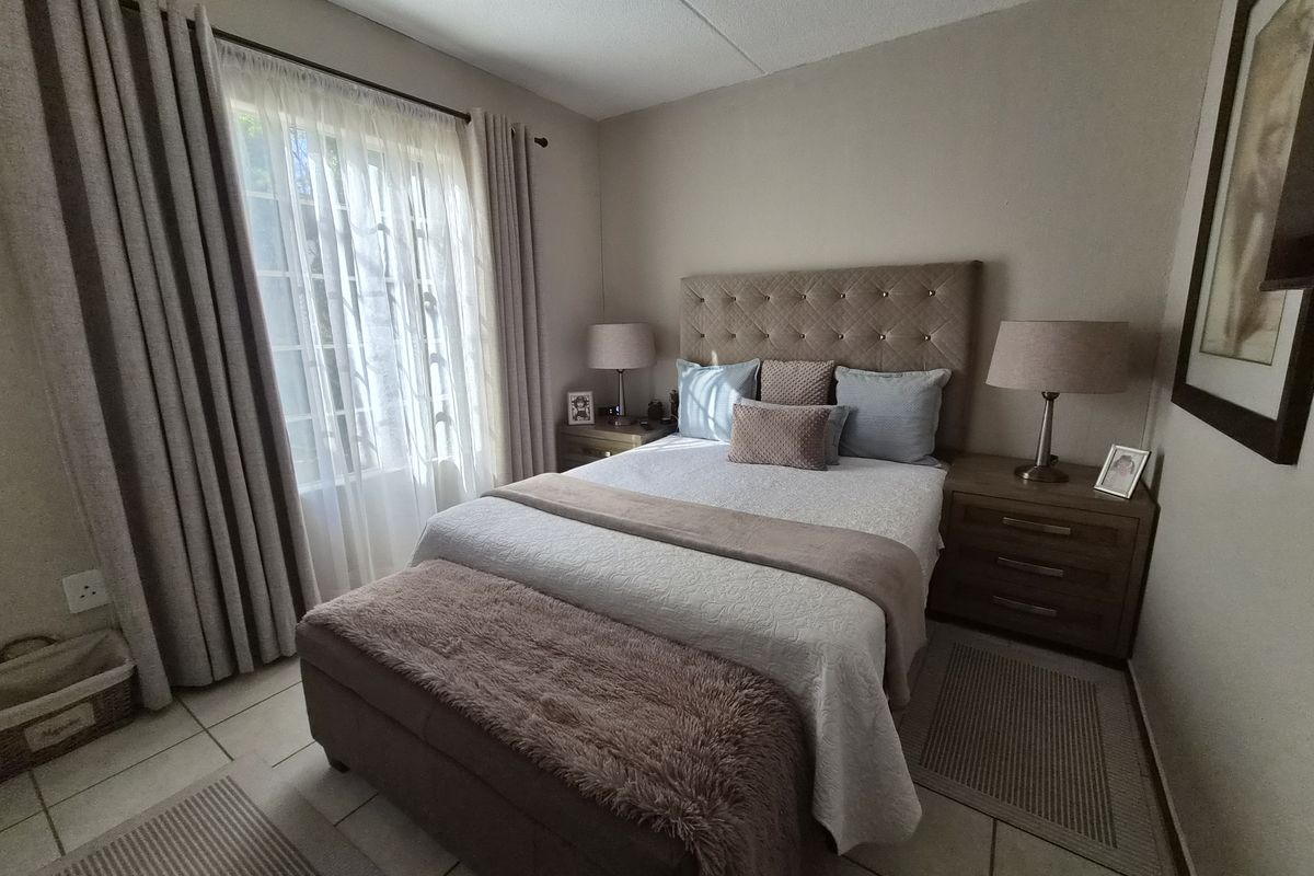 A well-maintained bedroom featuring neutral wall tones, tiled flooring, and large windows with curtain treatments, providing a comfortable and functional living space.