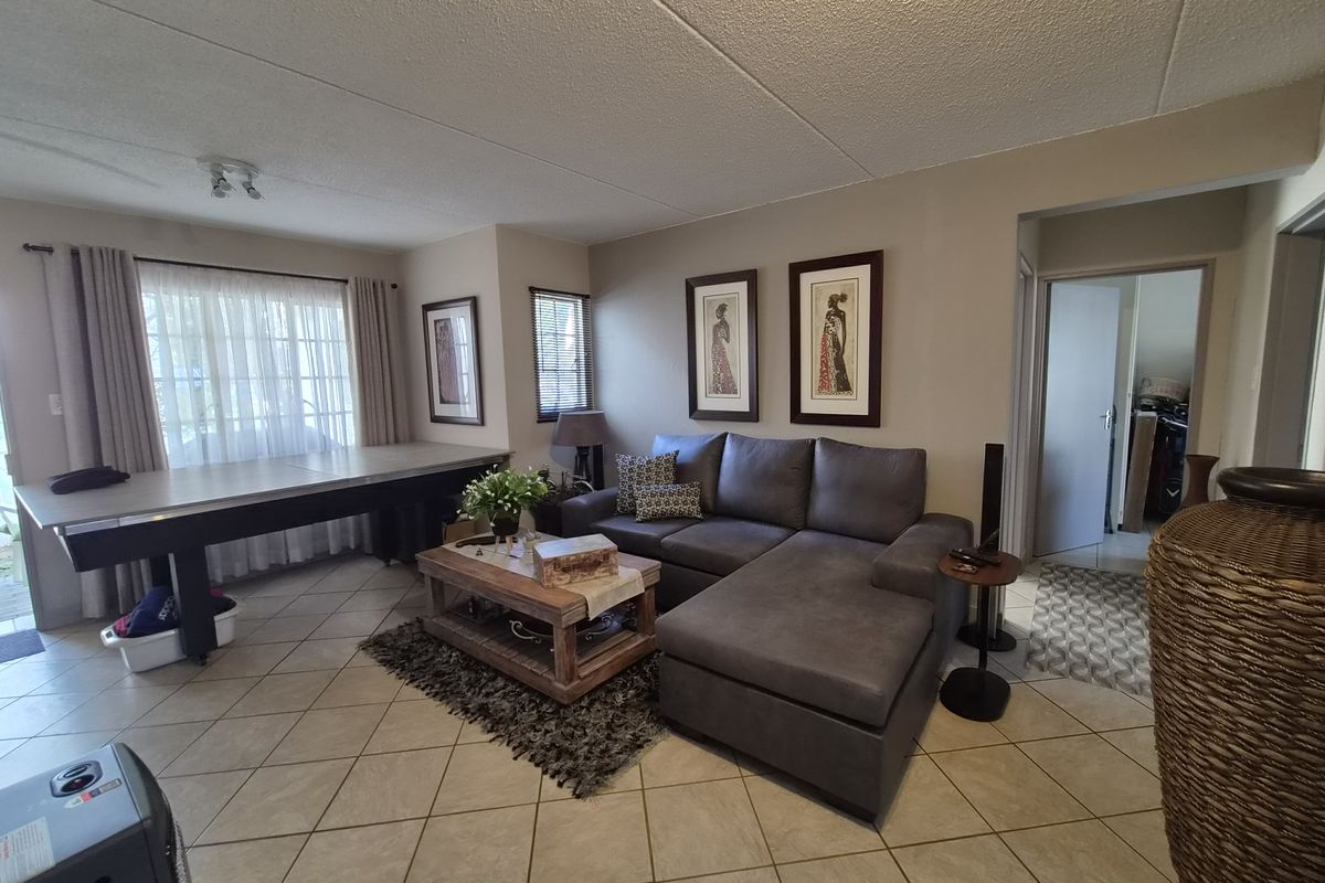 A spacious living room featuring neutral ceramic floor tiles, a textured ceiling, and large sliding glass doors that provide natural light.