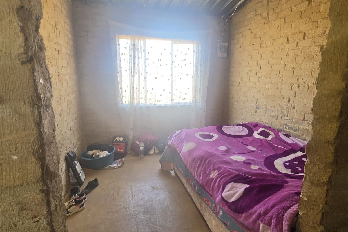A basic bedroom featuring exposed brick walls and a corrugated metal ceiling, providing a rustic, unfinished aesthetic.