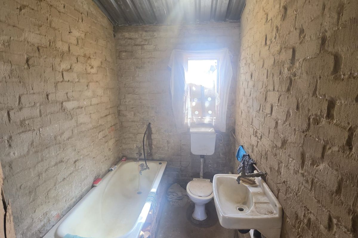 A basic bathroom featuring exposed brick walls, a corrugated metal ceiling, a bathtub, a toilet, and a wall-mounted basin in need of renovation.