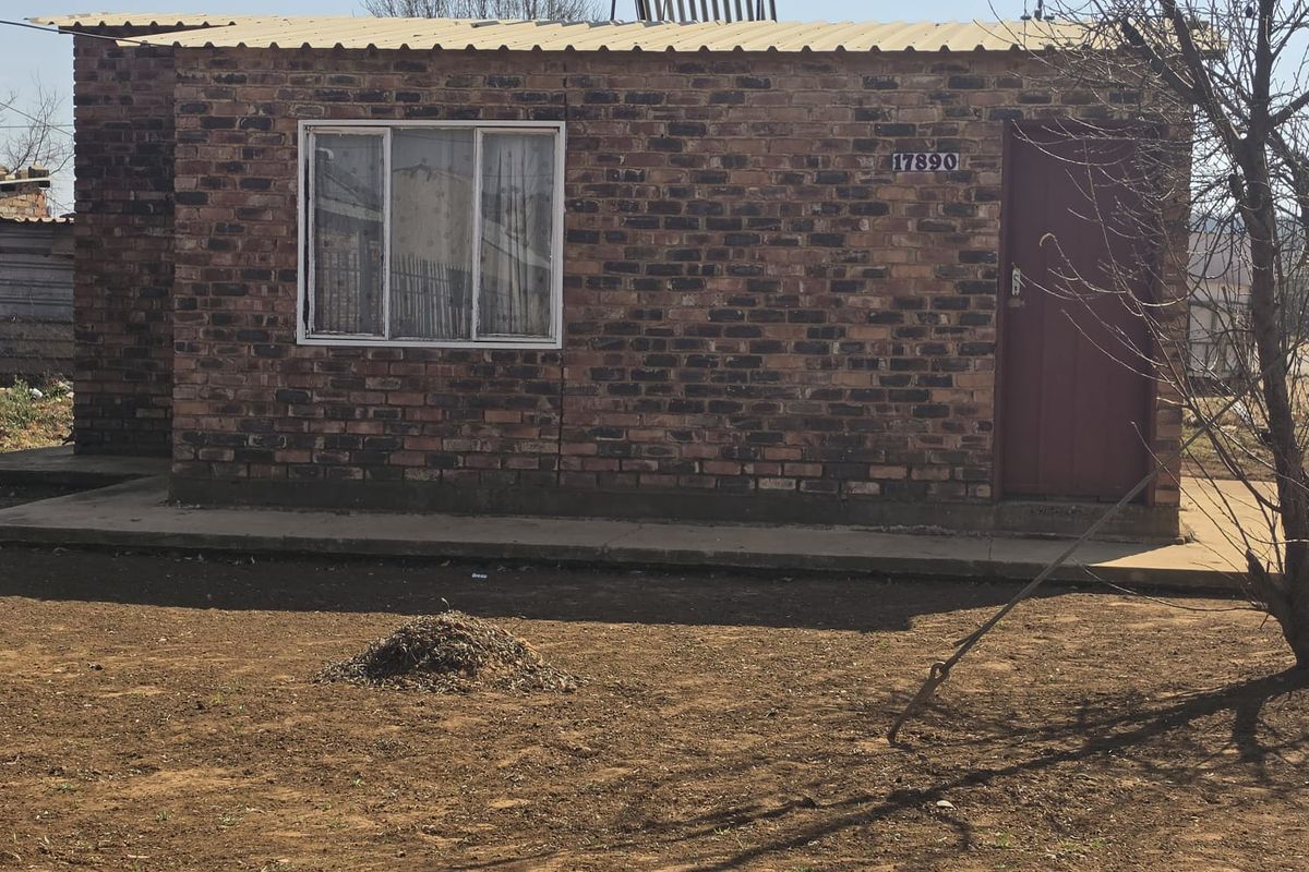 Front view of a single-story exposed brick house featuring a solar water heater and a concrete apron entrance.