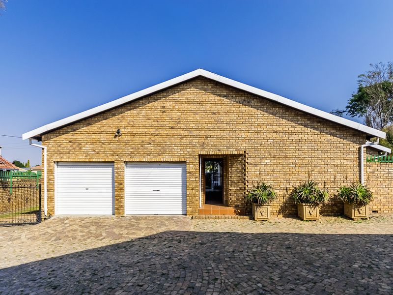 Front view of a brick-faced duet property featuring a double garage, paved driveway, and secure boundary walling.