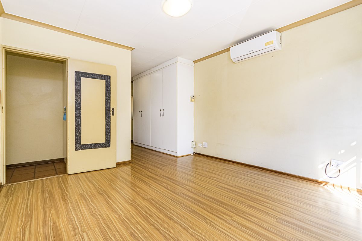 A spacious, empty bedroom featuring laminate flooring, built-in cupboards, and a wall-mounted air conditioning unit.