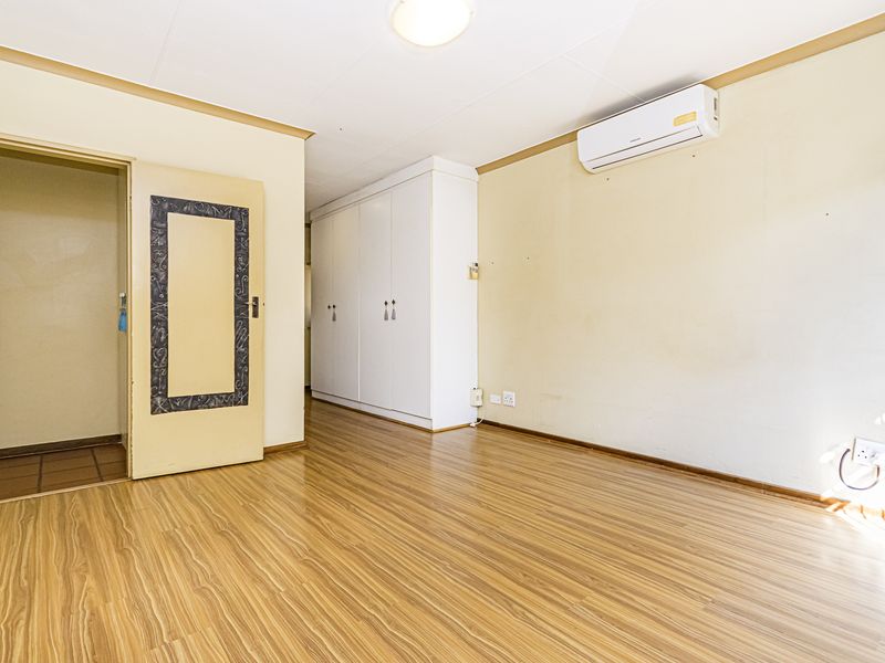 A spacious, empty bedroom featuring laminate flooring, built-in cupboards, and a wall-mounted air conditioning unit.