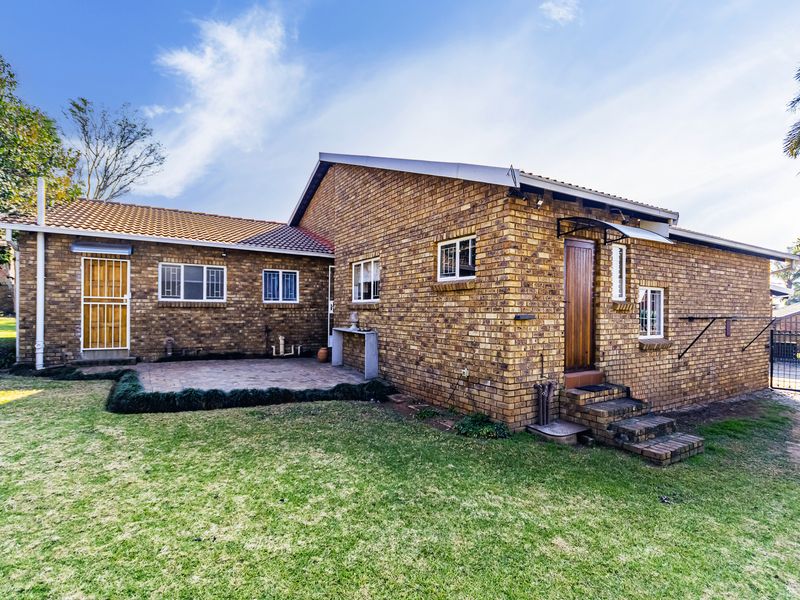 Rear view of the duet property featuring a facebrick facade, tiled roof, and a paved patio area leading into the garden.