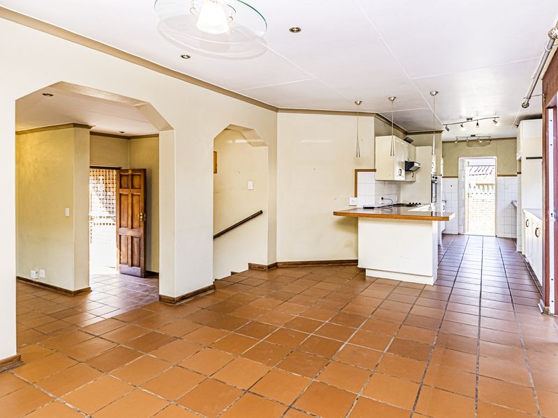 Spacious open-plan living and kitchen area featuring terracotta floor tiles, built-in cabinetry, and a breakfast counter, offering a versatile layout for modern living.