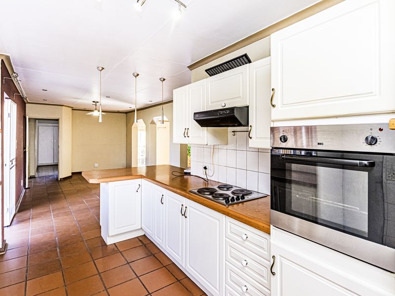 A functional kitchen featuring white cabinetry, wooden countertops, a built-in oven, and an electric hob, with tiled flooring throughout the open-plan space.