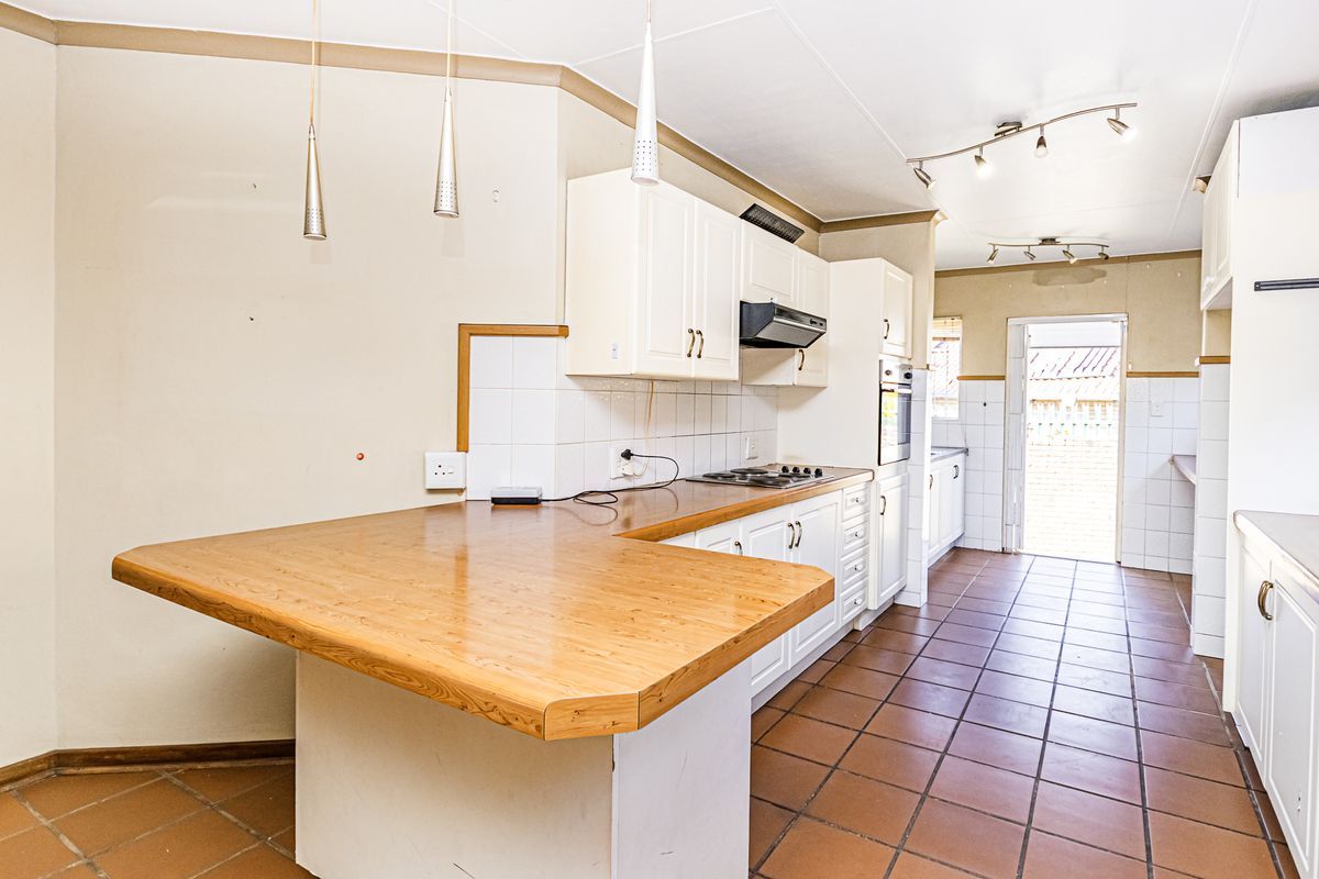 A spacious kitchen featuring white built-in cabinetry, a wooden breakfast counter, tiled flooring, and direct access to the exterior.