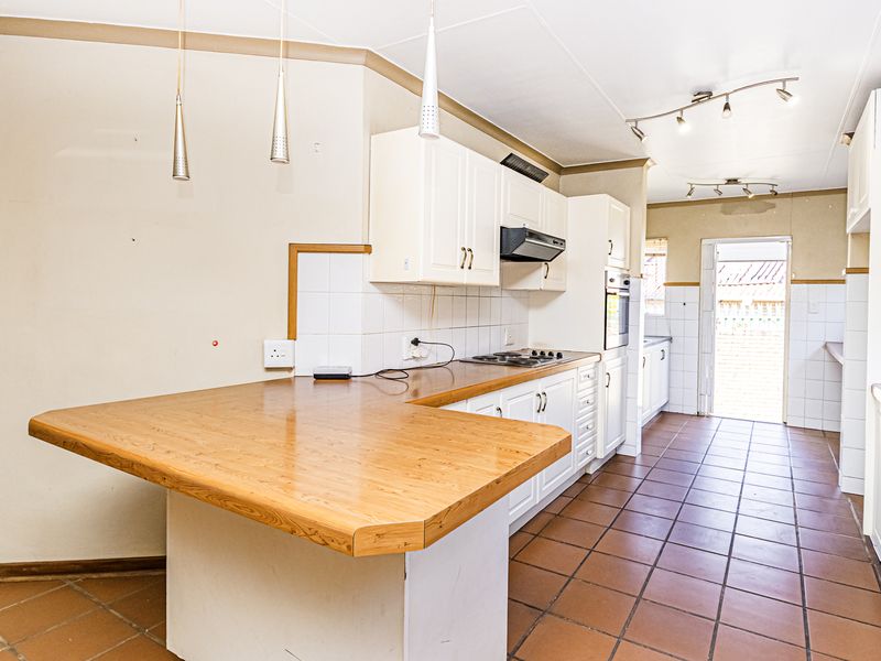 A spacious kitchen featuring white built-in cabinetry, a wooden breakfast counter, tiled flooring, and direct access to the exterior.