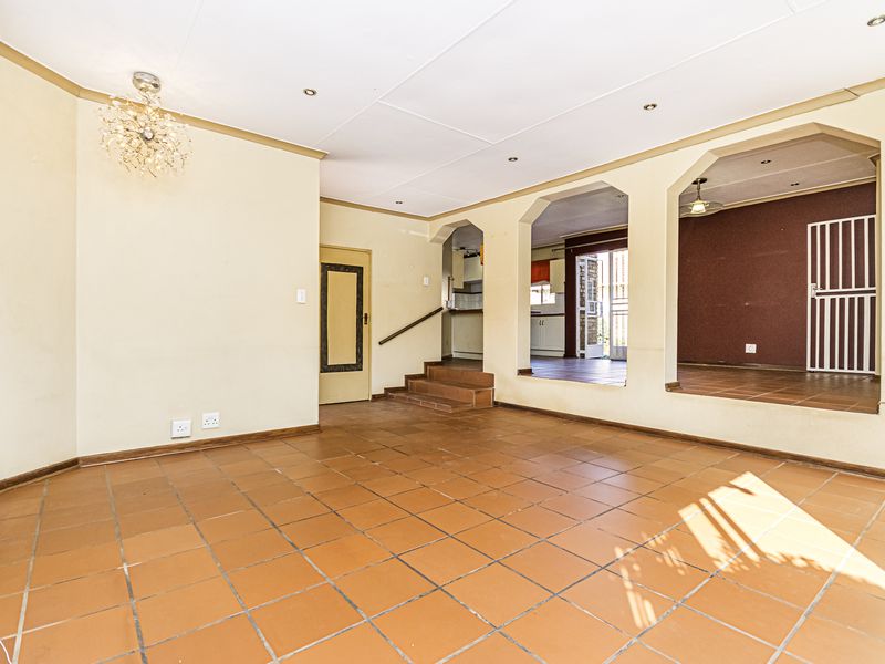 Spacious open-plan living area featuring terracotta floor tiles, recessed lighting, and distinct archway transitions leading to adjacent rooms.
