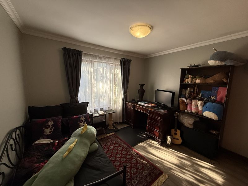 A bedroom featuring laminate flooring, ceiling cornice, and a central flush mount light fixture, offering a functional space with natural light.