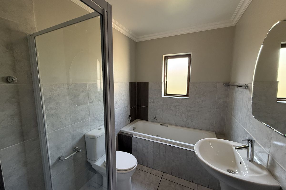 A clean, modern bathroom featuring a glass shower enclosure, a bathtub, a pedestal basin, and neutral tiled finishes throughout.