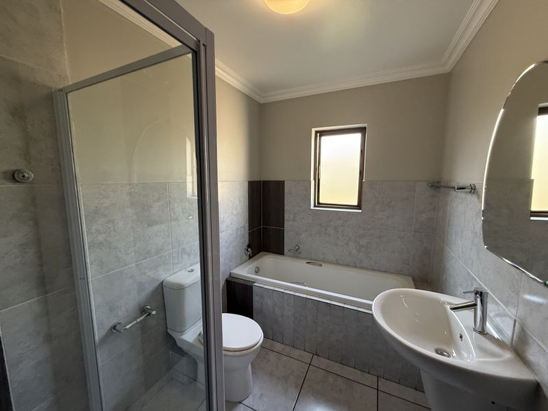 A clean, modern bathroom featuring a glass shower enclosure, a bathtub, a pedestal basin, and neutral tiled finishes throughout.