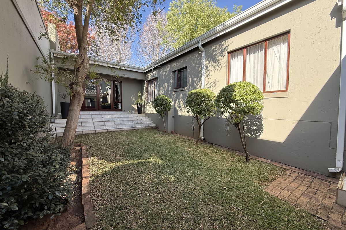 A private rear courtyard featuring a small lawn, brick paving, and tiled steps leading to timber-framed sliding doors.