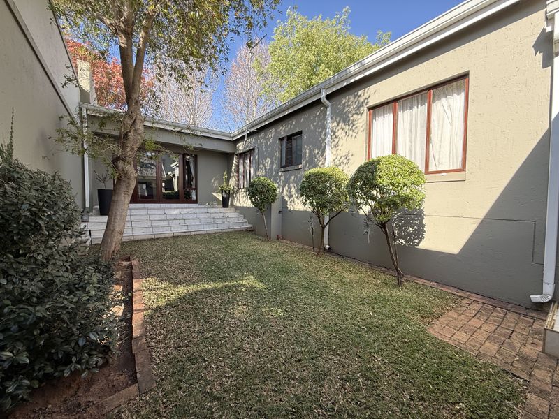 A private rear courtyard featuring a small lawn, brick paving, and tiled steps leading to timber-framed sliding doors.