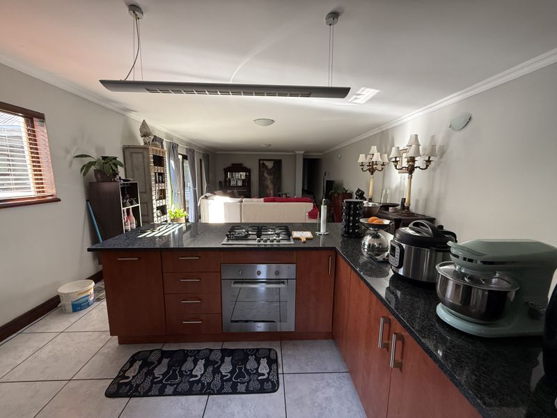 Open-plan kitchen featuring granite countertops, built-in oven, gas hob, and wooden cabinetry, flowing into the adjacent living area with tiled flooring.
