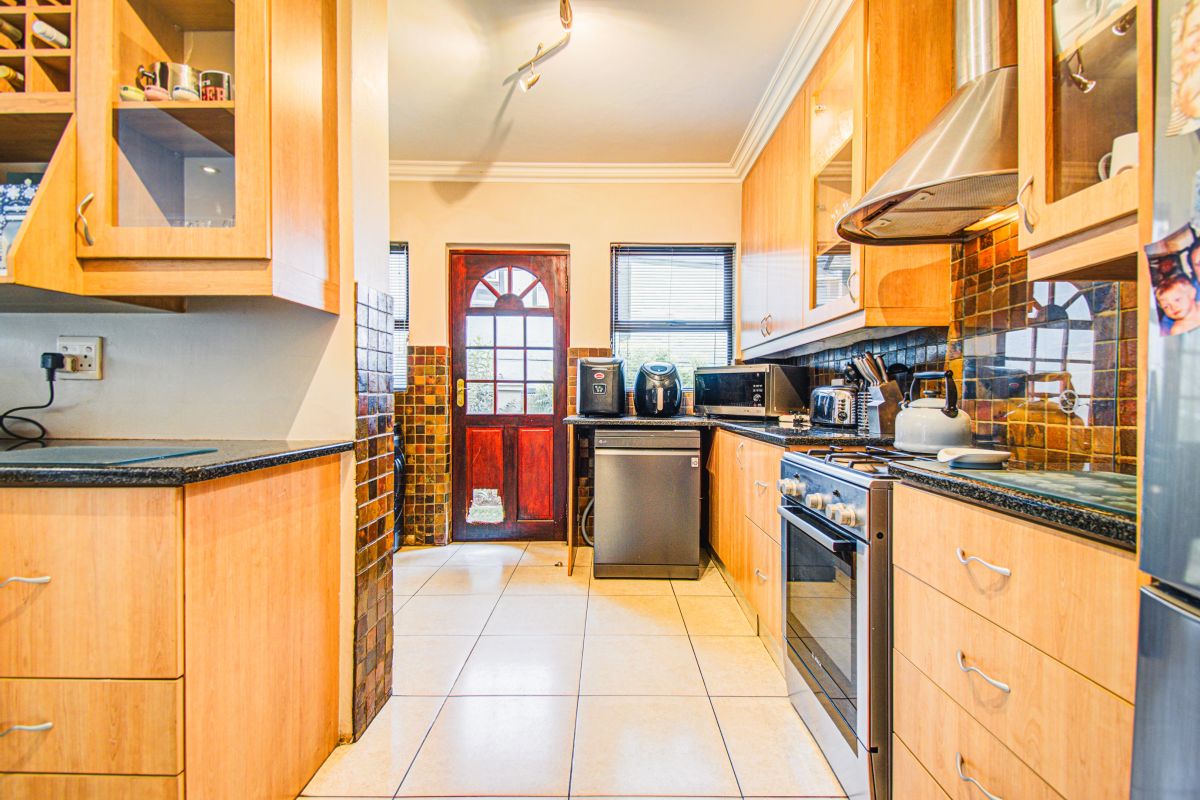 A functional kitchen featuring wooden cabinetry, granite countertops, a stainless steel extractor fan, gas stove, and tiled flooring with direct access to the exterior.