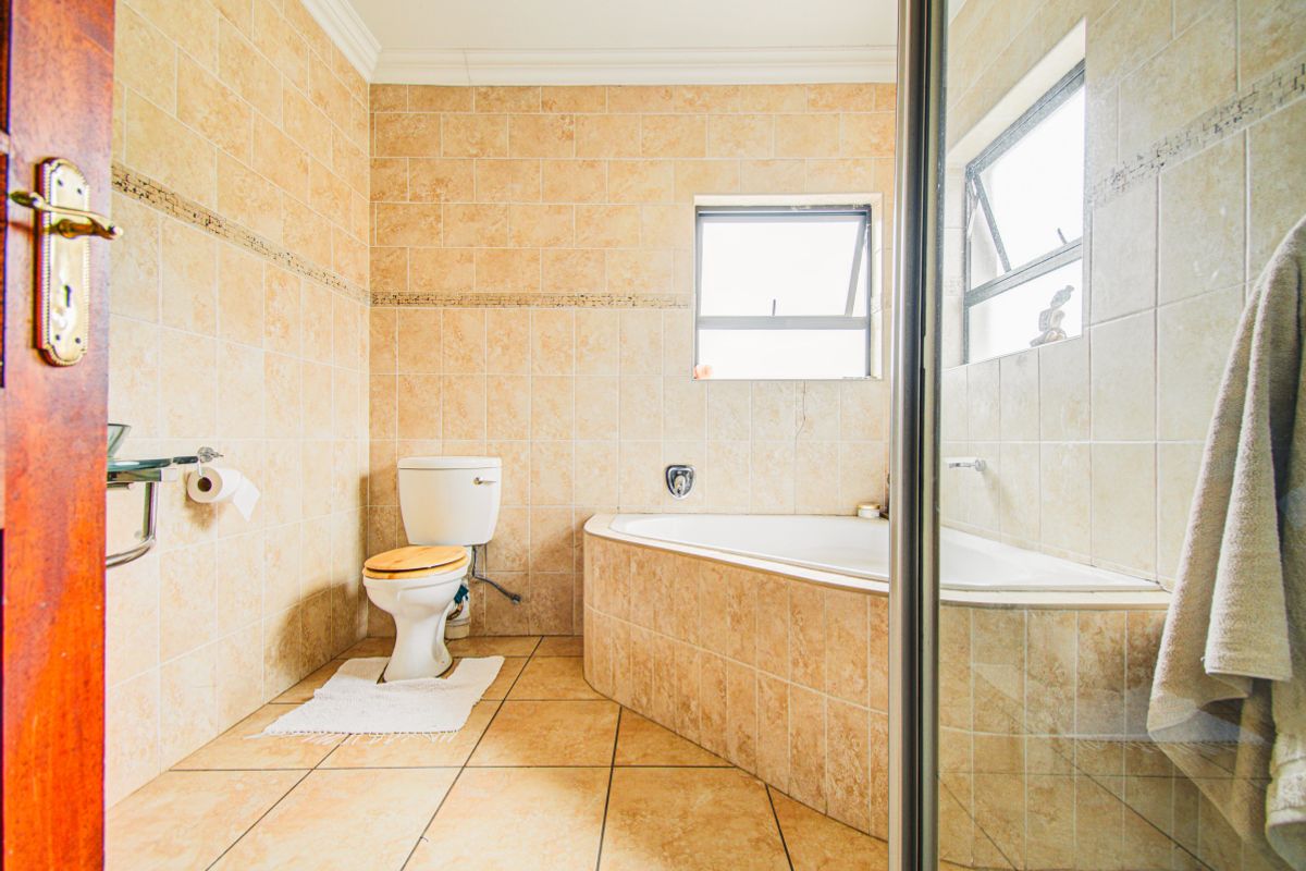 A functional bathroom featuring a corner bathtub, tiled walls and flooring, and a separate shower enclosure with natural light from a top-hung window.