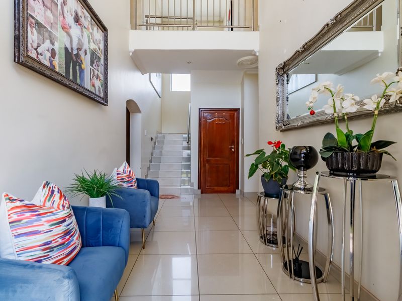 Spacious entrance hall featuring polished floor tiles, a staircase with a metal balustrade, and a solid wood front door.