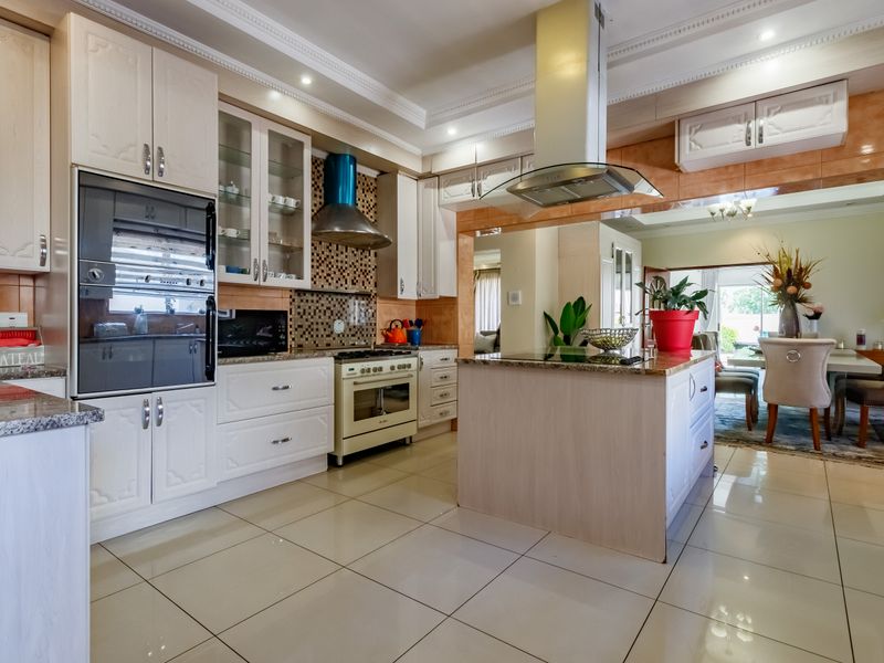 Spacious kitchen featuring light-toned cabinetry, granite countertops, a central island, and integrated appliances, flowing seamlessly into the adjacent dining area.