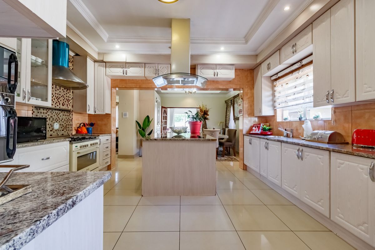 Spacious kitchen featuring granite countertops, built-in cabinetry, a central island, and a stainless steel extractor fan, flowing into the adjacent dining area.