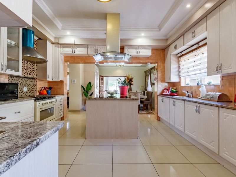 Spacious kitchen featuring granite countertops, built-in cabinetry, a central island, and a stainless steel extractor fan, flowing into the adjacent dining area.