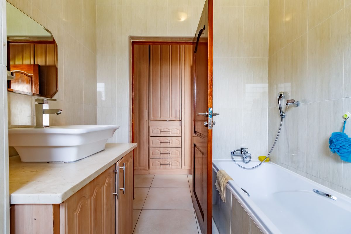 A functional bathroom featuring a vessel sink on a vanity cabinet, a bathtub with a handheld shower, and integrated built-in wardrobe storage.