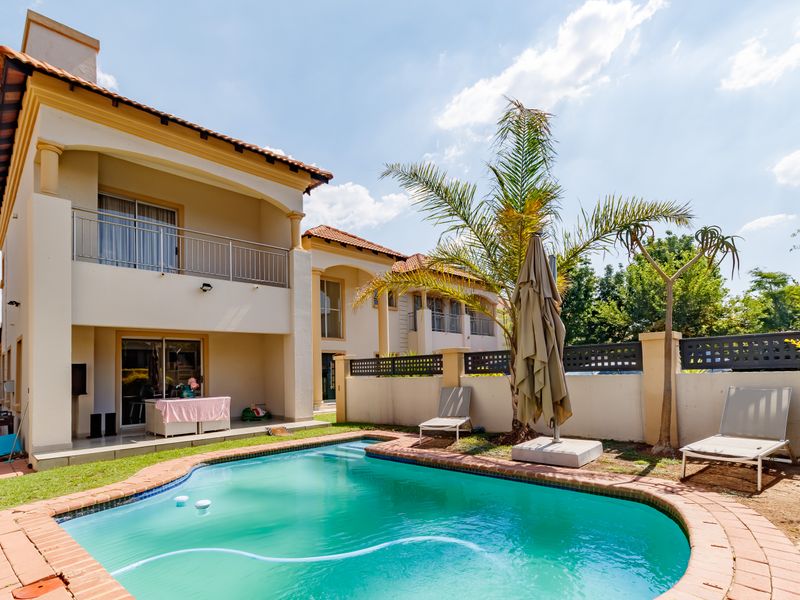 Rear view of the property featuring a swimming pool with brick coping, a covered patio, and an upper-level balcony with metal railings.