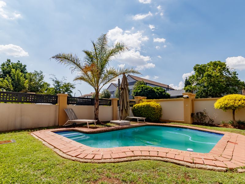 A private backyard featuring a swimming pool with brick coping, surrounded by a perimeter wall and landscaped garden area.