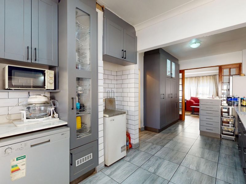 Modernized kitchen featuring grey shaker-style cabinetry, subway tile backsplash, and tiled flooring, with an open-plan layout leading to the adjacent living area.