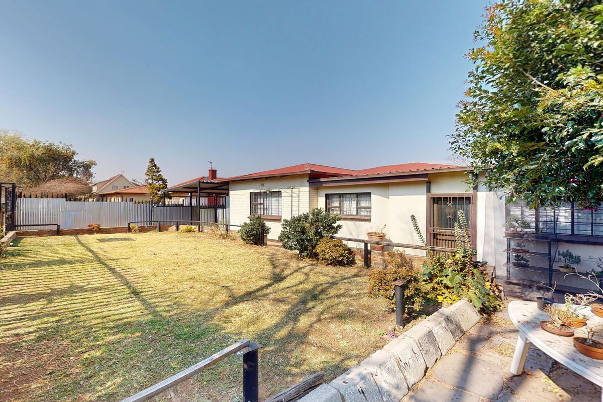 Rear view of the house featuring a spacious lawn, paved patio area, and secure perimeter fencing with security bars on windows.