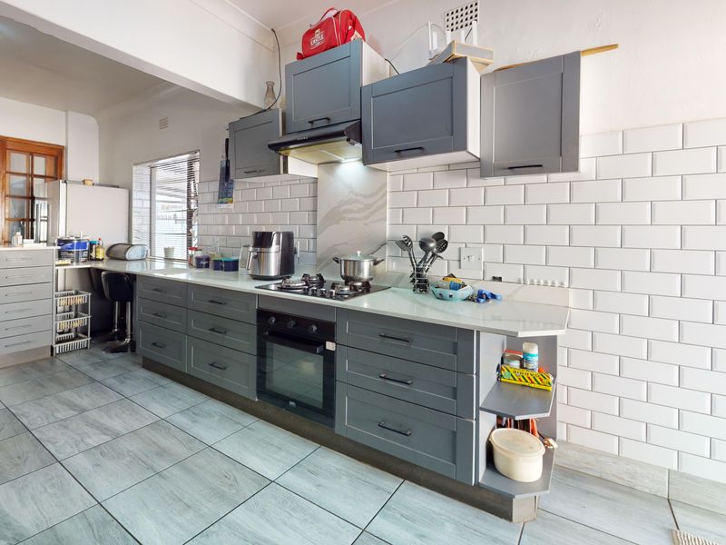 Modern kitchen featuring grey cabinetry, subway tile backsplash, built-in oven, gas hob, and stone countertops with tiled flooring.