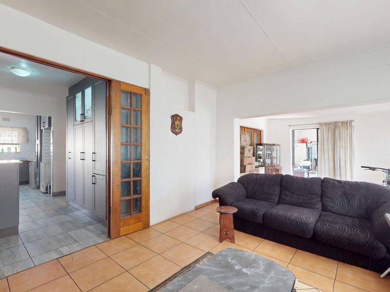 Open plan living area featuring tiled flooring and a timber framed glass door leading to a kitchen space with built-in cabinetry.
