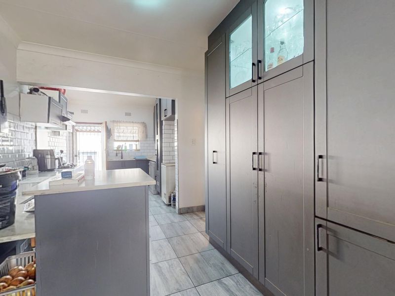 Modern kitchen featuring dark grey cabinetry, subway tile backsplash, stone countertops, and integrated storage solutions with glass-front display units.