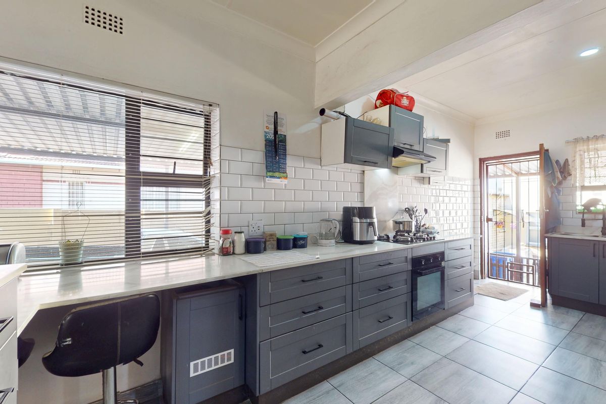 Modern kitchen featuring grey cabinetry, subway tile backsplash, stone countertops, built-in oven, and gas hob with direct access to the exterior.