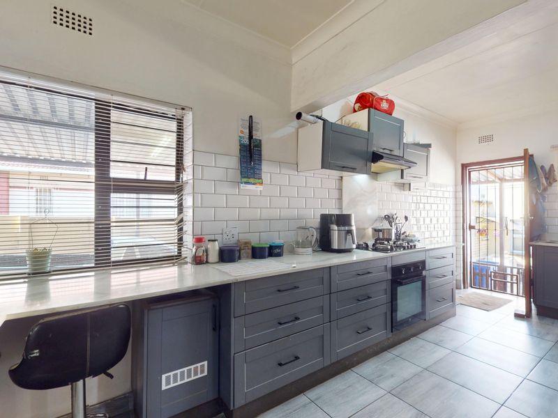 Modern kitchen featuring grey cabinetry, subway tile backsplash, stone countertops, built-in oven, and gas hob with direct access to the exterior.