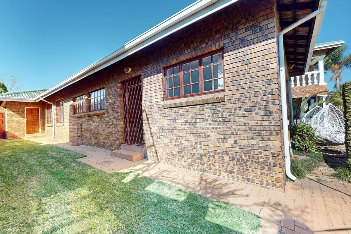 A view of the rear exterior of the house featuring a face brick facade, paved walkway, and a well-maintained lawn.